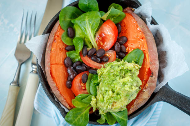 Baked whole sweet potato with guacamole and black beans in a cast-iron frying pan.