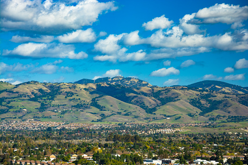 Diablo Range mountain range view from San Jose in Santa Clara County / Silicon Valley with the peak of Mount Hamilton in view just behind (with Lick Observatory at the top) and with a blue sky with clouds above.