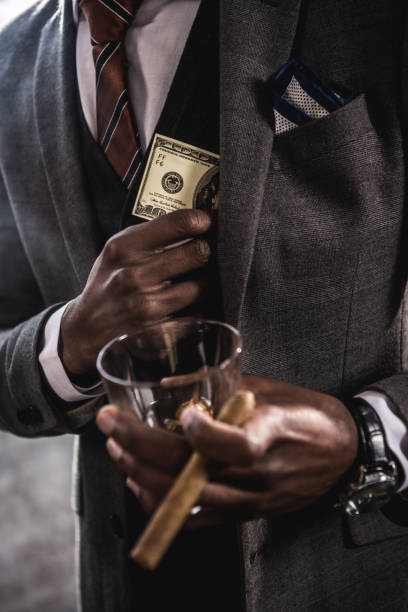 gros plan vue partielle de l’homme d’affaires américain tenant le verre de boisson de l’alcool et le cigare tout en cachant dollar billet dans poche de veste de costume - pocket suit close up shirt photos et images de collection