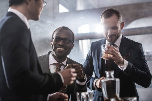 Multiethnic group of businessmen spending time together drinking whiskey and smoking, multicultural business team