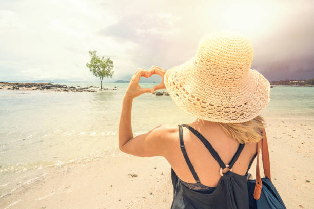 istock Woman making heart shape frame on tropical beach landscape 691437268