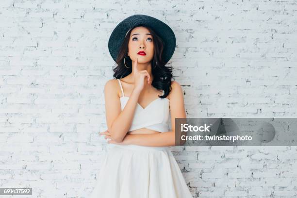 Young Woman Thinking About Something With Fashionable Summer Hat Over White Wall Background With Copy Space Stock Photo - Download Image Now