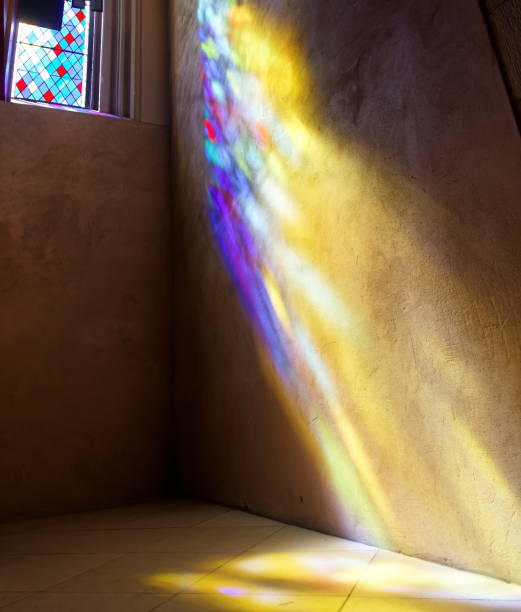 Sun rays coming from the center of a stained glass window with a cross.