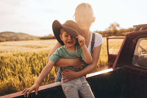 Photo of young mother bonding with her boy by taking him outdoors in the nature, while doing errands on a family farm with their family pick up truck