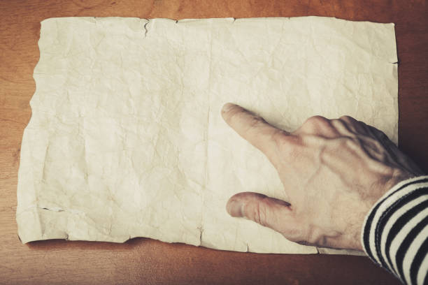 Sailors hand pointing some place on the empty old crumpled paper sheet, pirate map copy-space template. Vintage toned photo with selective focus