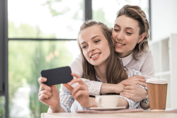 istock young smiling girlfriends embracing and taking selfie on smartphone at cafe 691483436