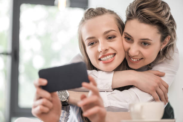 istock young smiling girlfriends embracing and taking selfie on smartphone at cafe 691483790