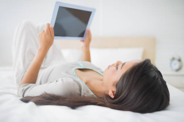 Pretty young girl lying on bed looking at her tablet pc in her bedroom at home