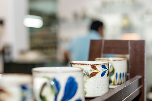 A saleswoman points at a plate being sold in a display of homemade pottery at a local small business owners shop.  Various cups and mugs can be seen in the back ground on glass display shelves.A saleswoman points at a plate being sold in a display of homemade pottery at a local small business owners shop.  Various cups and mugs can be seen in the back ground on glass display shelves.