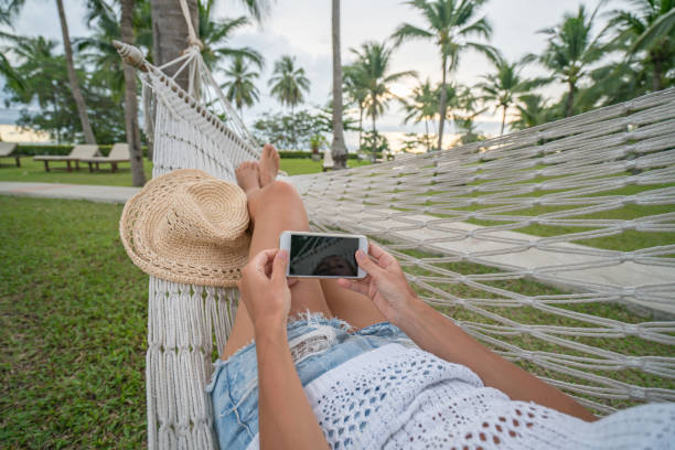 istock Young woman lying on white hammock relaxing with a smart phone 691504100