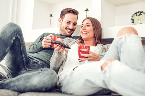 Couple in love enjoying their free time, sitting on a couch,drinking coffee and watching TV