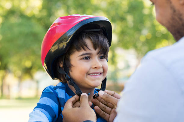 Boy wearing cycle helmet Father helping cheerful son wearing helmet for cycle. Excited little boy getting ready by wearing bike helmet to start cycling. Happy cute boy learn to ride a bike with his dad. cycling helmet photos stock pictures, royalty-free photos & images
