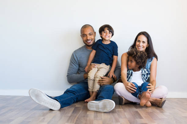 Happy family with childreen Happy multiethnic family sitting on floor with children. Smiling couple sitting with two sons and looking at camera. Hispanic mother and black father relaxing with their cute boys leaning on wall with copy space. young family photos stock pictures, royalty-free photos & images