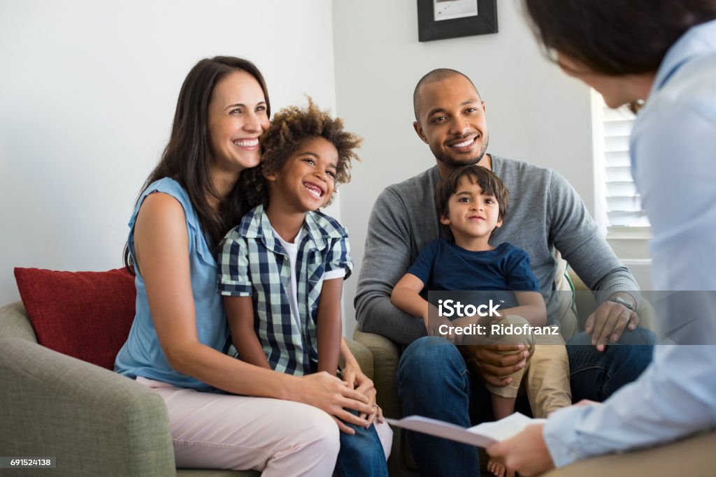 Family talking with counselor Happy young family sitting on couch and talking with family counselor. Smiling parents with adopted children discussing with counselor. Multiethnic family meeting a financial agent. Family Stock Photo