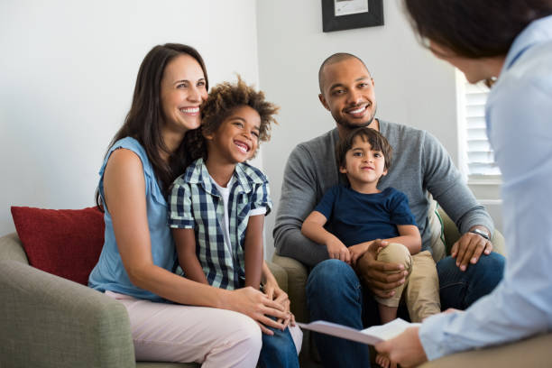 Family talking with counselor Happy young family sitting on couch and talking with family counselor. Smiling parents with adopted children discussing with counselor. Multiethnic family meeting a financial agent. insurance agent photos stock pictures, royalty-free photos & images