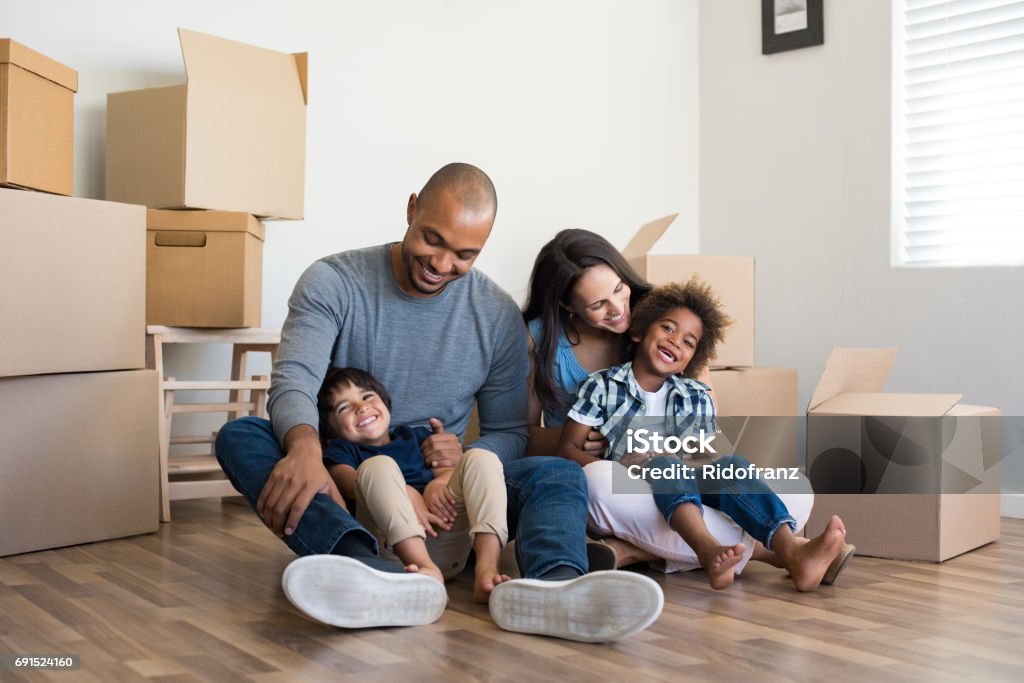 Multiethnic family moving home Happy family with two children having fun at new home. Young multiethnic parents with two sons in their new house with cardboard boxes. Smiling little boys sitting on floor with mother and dad. Family Stock Photo