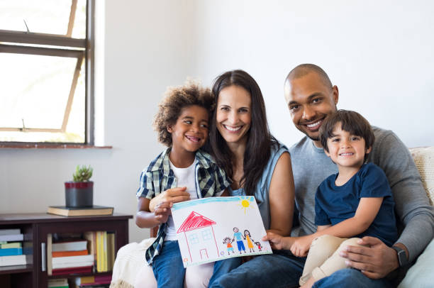 Multiethnic family on sofa Proud parents showing family painting of son sitting on sofa at home. Smiling mother and father with children"u2019s drawing of a new home. Black little boy with his family at home showing a painting of a happy multiethnic family. multiracial person stock pictures, royalty-free photos & images