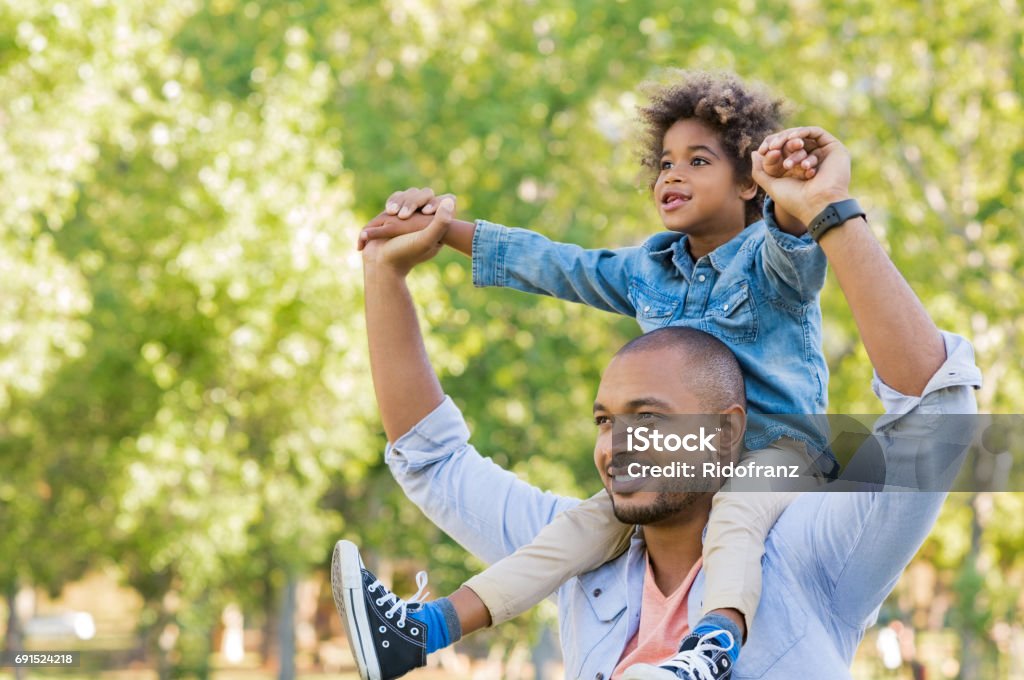 Black father and son vision Father giving son ride on back at park. Portrait of happy african father giving son piggyback ride on his shoulders and looking up. Cute black boy with dad playing outdoor. Father day concept. Child Stock Photo