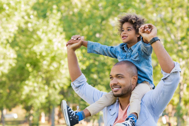 Black father and son vision Father giving son ride on back at park. Portrait of happy african father giving son piggyback ride on his shoulders and looking up. Cute black boy with dad playing outdoor. Father day concept. on shoulders stock pictures, royalty-free photos & images
