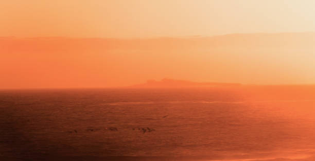 view of the sea with rocks on the background. Soft focus makes it hard to differentiate the water from sand making the image look like the view of a desert town in the back with bright sunlight and sand storm, but it actually was the fog.