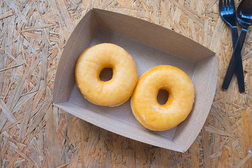 Delicious donuts in brown paper box on wood table