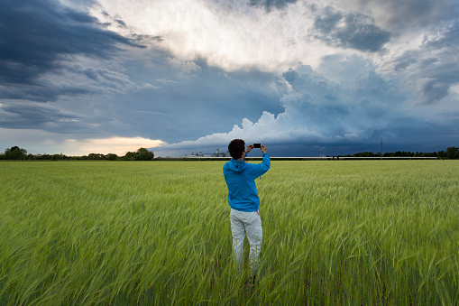 Outdoor shot of a boy taking picture with smart phone of incoming storm