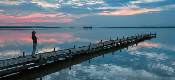 silhouette di donna in piedi sul molo al lago a guardare scenografie idilliache al crepuscolo - steinhuder meer foto e immagini stock