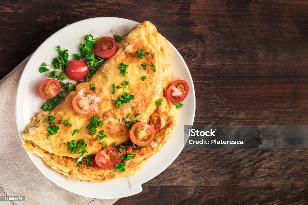 Omelet with parsley, cherry tomatoes, and copyspace A photo of an omelet with cherry tomatoes, parsley. and grated cheese, shot from above on a rustic wooden texture with a place for text Omelet Stock Photo