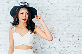 白いレンガの壁でおしゃれなドレスと夏帽子笑顔若い幸せなアジア女