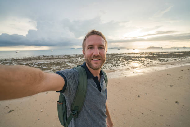istock Young man traveling takes selfie on beach at sunset 691558728