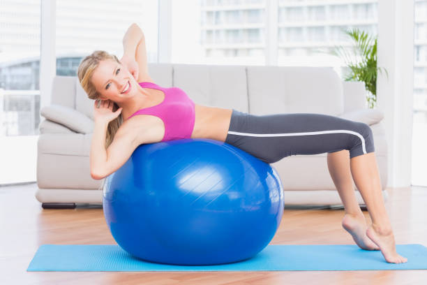 slim loira fazer sentar-ups na bola de exercício sorrindo para a câmera - pilates women sit ups yoga - fotografias e filmes do acervo