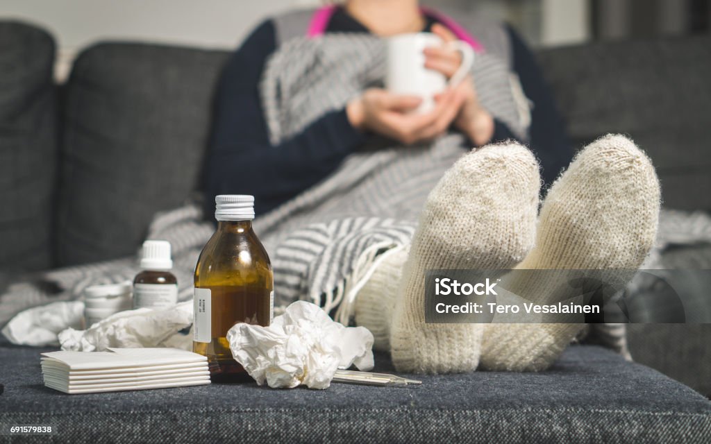 Remédio para gripe e mulher doente beber bebida quente para obter bom da gripe, febre e vírus. Toalhas de papel sujo e lenços na mesa. Pessoa doente vestindo meias de lã quente meias no inverno. - Foto de stock de Resfriado e Gripe royalty-free