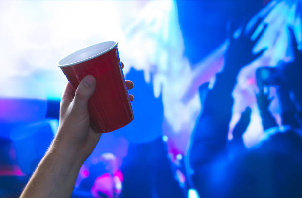 jeune homme tenant la coupe du parti rouge en piste de danse discothèque. conteneur d’alcool dans la main dans la discothèque. étudiant universitaire, s’amuser et danser. fête des gens dans le dos. marketing événementiel et la promotion. - disposable cup red beer plastic photos et images de collection