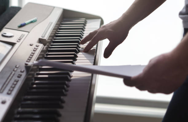 istock One single finger pressing key on piano. Man looking at paper notes and training a new song or melody from the sheet music. Pianist composing new work or creative producer working in home studio. 691580182