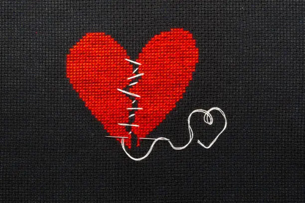 Photo of Two halves heart embroidered red thread on black fabric. Two halves heart sewn with black thread.