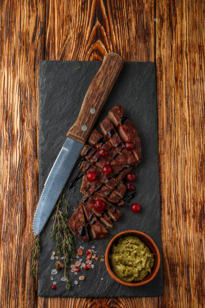 istock Grilled sliced beef steak with cranberry, balsamic vinegar, thyme and spices on a slate plate. The pesto sauce. Top view 691603244