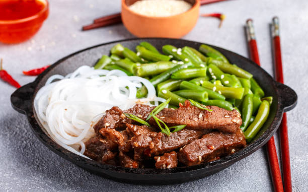Fried spicy beef with sesame seeds, green beans and rice noodles. Dinner in the Asian style. Selective focus