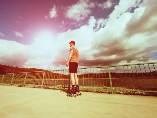 Vintage tone filter effect color style. Sportsman  with inline skates ride in summer park close to handrail, outdoor roller skater on park bridge