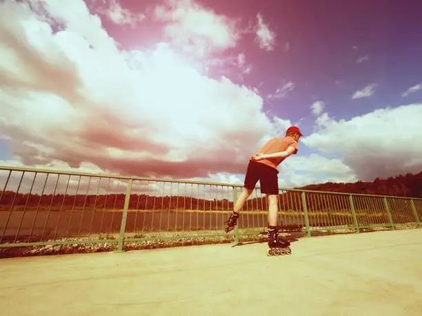 Vintage tone filter effect color style. Sportsman  with inline skates ride in summer park close to handrail, outdoor roller skater on park bridge