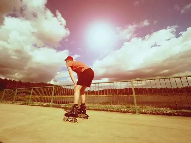 Vintage tone filter effect color style. Sportsman  with inline skates ride in summer park close to handrail, outdoor roller skater on park bridge