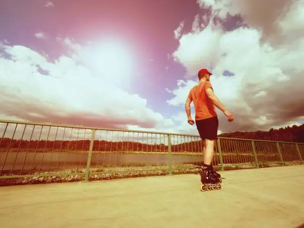 Vintage tone filter effect color style. Sportsman  with inline skates ride in summer park close to handrail, outdoor roller skater on park bridge