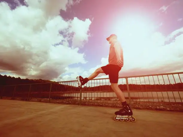 Vintage tone filter effect color style. Sportsman  with inline skates ride in summer park close to handrail, outdoor roller skater on park bridge