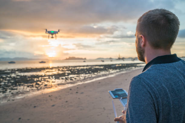 istock Young man piloting a drone on tropical beach at sunset 691623450