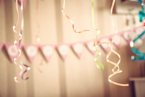 Retro styled happy birthday party blurred background with hanging ribbons and garland in decorated room in pastel colors