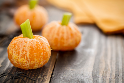 Healthy Halloween snacks for kids.  Tangerine jack o'lanterns made of tangerines and celery stick with spider decoration.  These healthy halloween are fun food for kids on rustic wood table.