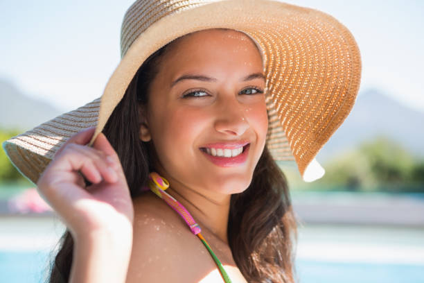 istock Beautiful brunette sitting by pool wearing straw sunhat 691656154