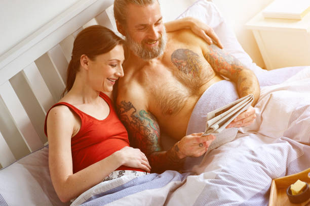 ベッドで新聞を読んで幸せな妊娠中のカップル - newspaper reading mother women ストックフォトと画像