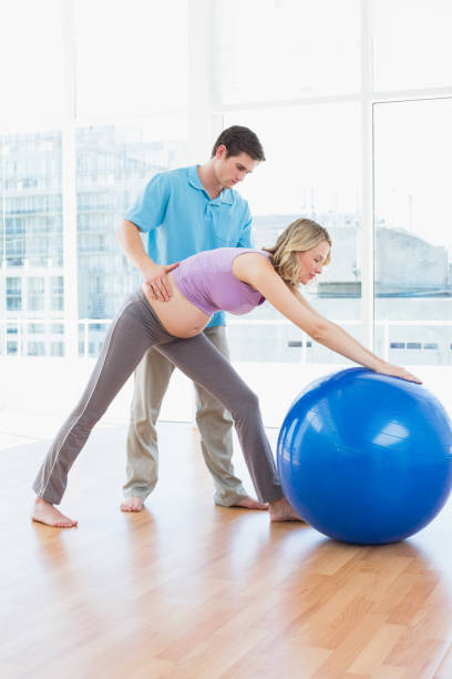 istock Trainer exercising with pregnant client and exercise ball 691672660