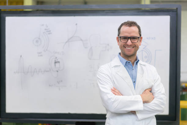 Portrait of a happy engineering teacher at the university Portrait of a happy engineering teacher at the university in front of a whiteboard looking at the camera smiling - education concepts industrial designer stock pictures, royalty-free photos & images