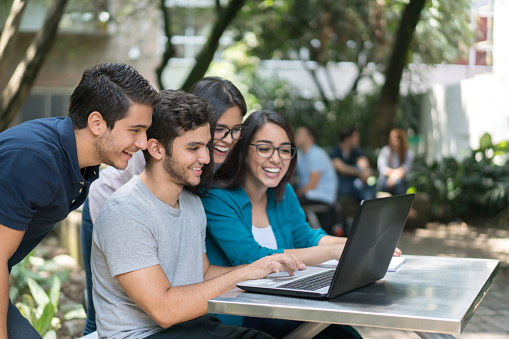 Portrait of a happy group of students at the university using a laptop computer while studying outdoors - education concepts